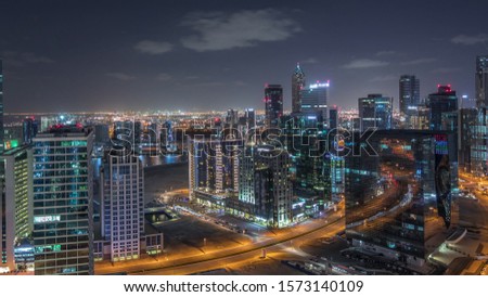 Business bay illuminated towers with parking at night timelapse. Rooftop view of some skyscrapers near canal and new towers under construction with crane. Traffic on roads and lights in windows