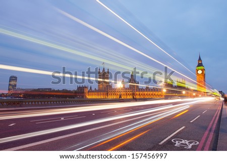 Traffic through London. Big Ben, one of the most prominent symbols of both London and England, as shown at night along with the lights of the cars and busses passing by