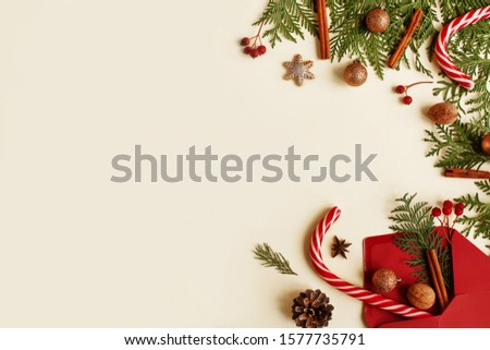 Christmas or New Year light background with a frame on the right side of the festive decor: Christmas tree twigs, balls, spices, gingerbread cookies and Christmas canes. Empty space for text, flat lay