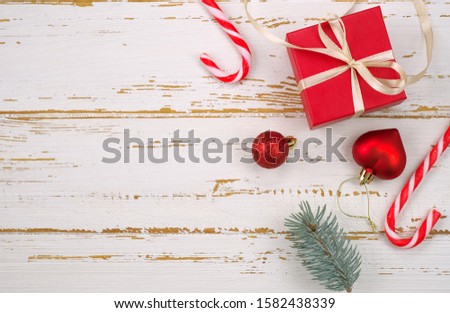 Red gift box with a Christmas toy in the shape of a heart, fir branches, christmas candy, garland and card for congratulatory text  on the wooden background. Top view. Flat lay