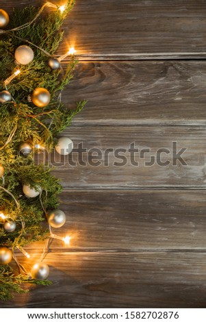 Christmas holiday lights, green pine, and golden yellow ornaments on a wooden background. Graphic design background