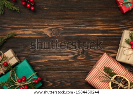 Chrristmas background with gift boxes wrapped in eco paper with ropes, decorated with spruce branches and holy berries on natural wood background . Holiday preparations, frame with space for text