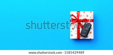 Give gift car key concept top view. Present box with red ribbon bow, heart and car key on blue colored background.