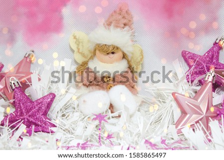 Plush fabric Christmas ornament little girl angel and star-shaped ornaments. Christmas still life.Stars baubles in purple tones and pink-white baby girl angel under the lights.