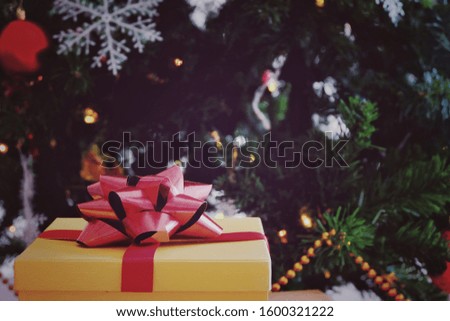   A yellow gift box, red ribbon in front Сhristmas tree Decoration dark background