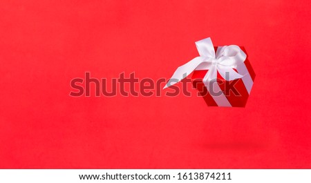 Banner red gift box with white satin ribbon bow flying on red background. Minimal concept for christmas holidays, birthday, valentine, shopping and sales.