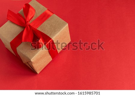 A gift for your beloved on Valentine's Day. DIY gift from kraft paper with a red satin ribbon on a red background. Birthday. March 8.
