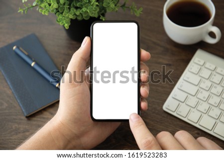 male hand holding phone with isolated screen over table in the office