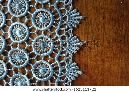 Vertical edge of light blue crochet lace on wooden table