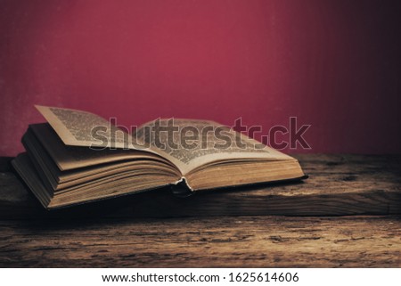 Old book on a old oak wooden table and red wall background behind.