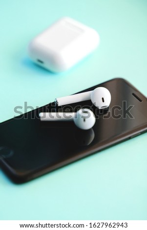 Smartphone and wireless earphones isolated on the blue background. 