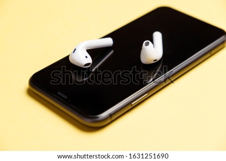 White modern wireless headphones lie on the smartphone display. Yellow background. Concept of modern technologies. Musical concept. Minimalism. Smart devices