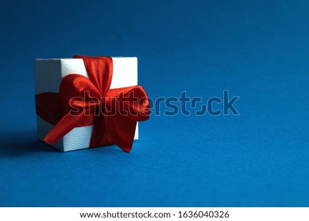 White gift box with red ribbon on blue background front view with copy space
