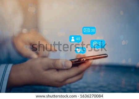 Person using a social media marketing concept on mobile phone with notification icons of like, message, comment above smartphone screen.