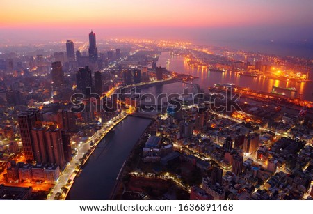 Aerial view of Downtown Kaohsiung at sunrise, a vibrant seaport city in South Taiwan, with the landmark 85 Sky Tower standing by the harbor and street lights dazzling under dramatic twilight sky
