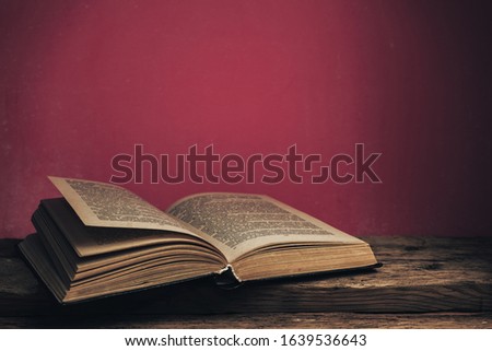 Close up Old book on a old oak wooden table and red wall background behind.