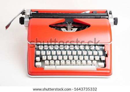A studio shot of a retro-style portable manual typewriter with ivory-color plastic keyboard and red-orange metal casing.
