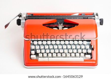 A studio shot of a retro-style portable manual typewriter with ivory-color plastic keyboard and red-orange metal casing.