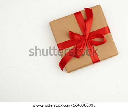 square box wrapped in brown kraft paper and tied with a red silk ribbon, white background, top view