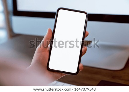 Woman holding smartphone mockup of blank screen and computer on the table office. Take your screen to put on advertising.