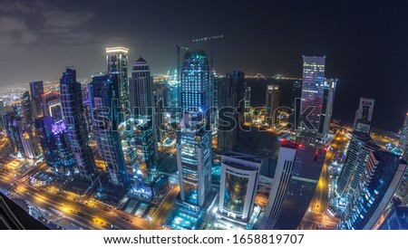 The skyline of the West Bay area from top in Doha timelapse, Qatar. Illuminated modern skyscrapers aerial view from rooftop at night. Traffic on the road. Fisheye lens
