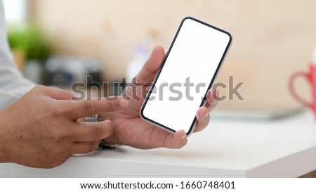 Close up view of male designer showing blank screen smartphone while sitting in simple workspace