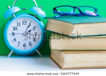 Stack of books with glasses and a vintage alarm clock.
