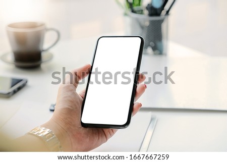 Woman hand holding smartphone on workplace. Blank screen mobile phone for graphic display montage
