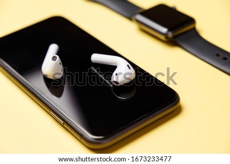 White modern wireless headphones lie on the smartphone display. Yellow background. Concept of modern technologies. Musical concept. Minimalism. Smart devices