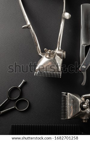 On a black surface are old hairdresser tools. Two vintage hand-held hair clippers, combs, razor, hairdressing scissors, shaving brush. black monochrome. vertical orientation.