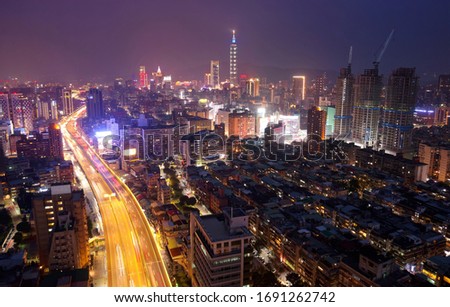 Night skyline of Downtown Taipei, the vibrant capital of Taiwan, with 101 Tower standing amid modern skyscrapers in Xinyi District & light trails of cars glowing on an elevated expressway at rush hour