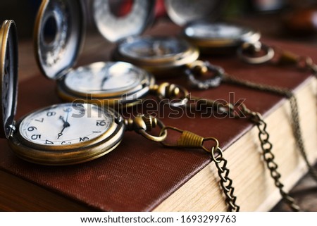 An image of four vintage pocket watches with chains on an antique book.