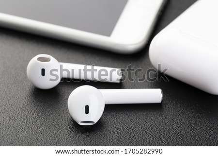 Wireless bluetooth headphones with a modern mobile phone on a dark background. The concept of modern technology, gadgets.
