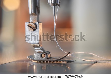 Needle presser foot with white thread of industrial sewing machine for sew cloth and blurred bokeh background with copy space close-up.