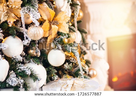 Decorated Christmas tree white and gold color, close-up of toys and decor, fireplace in background.