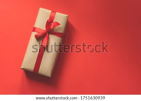 present box wrapped in plain paper with a red ribbon on red background with copy space