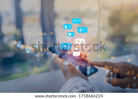 Woman hand using a social media marketing concept on mobile phone with notification icons of like, message, comment and star above mobile phone screen.