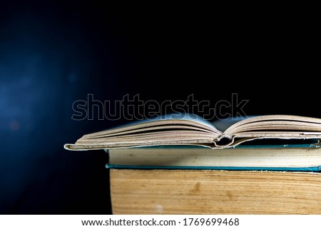 Opened old book on stack of books, dark background, space for text.