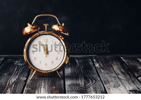 Gold alarm clock on a vintage wooden dark table. Rustic style. Selective focus, copy space. Time five minutes to twelve