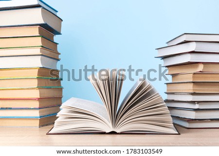 An open book and two stacks of books are on a wooden table against a light blue wall, free space for text