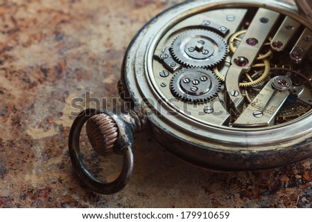 Close up view of the gears and mainspring in the mechanism of a silver pocket watch on old paper