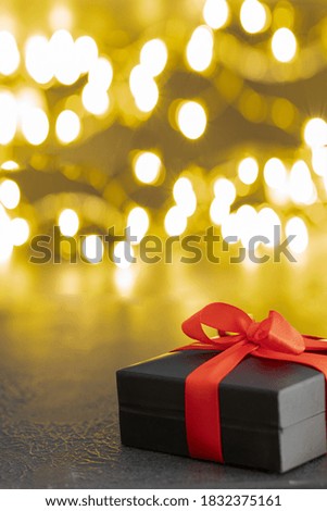 Black present box with red bow and sparkling garland  with bokeh on the back. 