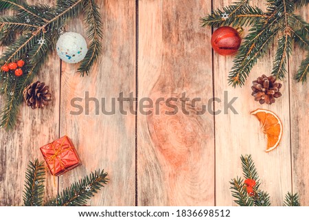 Christmas frame made of fir branches, red Rowan berries, red gift box, pine cones, Christmas balls, dried orange slices on a wooden background. Top view copy space. Beautiful Christmas background