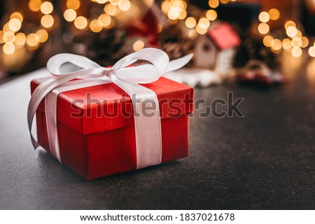 Red christmas square box with gift with white ribbon on table against bokeh background. Соpy space