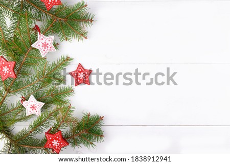Christmas background, natural fir tree branches with red and white wooden stars on a white wooden background, horizontal new year web banner top view. Reusable sustainable recycled decor.