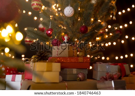Santa claus doll and stack of gift boxes under decorated christmas tree and bokeh lights background.