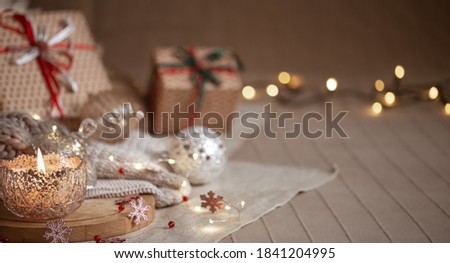 Christmas background with silver decorative burning candle, lights and gift boxes on a blurred background. Copy space.