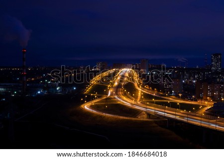 night urban landscape with illuminated road junction, residential buildings and an industrial zone with a chimney