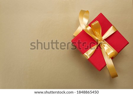 Red gift box with gold ribbon and bow on gold background
