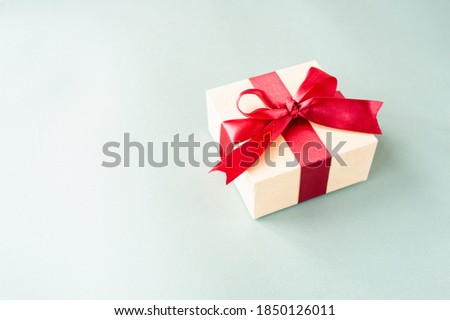 stylish square beige box with red festive satin ribbon on pastel blue background with space for text. Festive ready made layout, selective focus